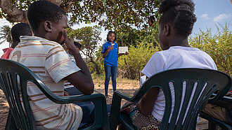 Ein Mädchen hält draußen einen Vortrag, vor ihr sitzen andere Jugendliche auf Plastikstühlen