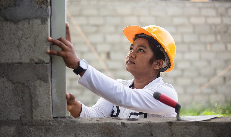 Dilara mit einem gelben Helm begradigt eine Mauer.