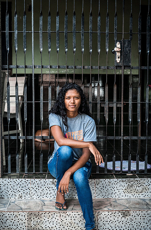 Eine junge Frau sitzt vor einem Tor auf einer Treppe.