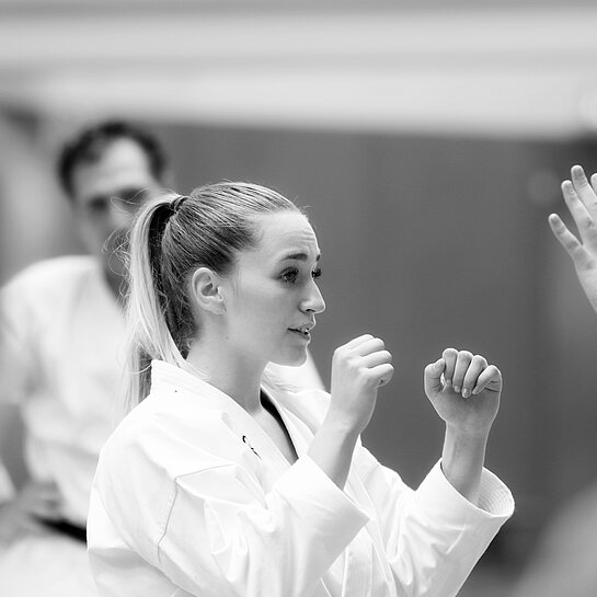 Eine Frau im Karate-Anzug hält die Arme kampfbereit vors Gesicht