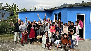 Gruppenfoto einer Projektreise in Nepal mit einem blauen Gebäude dem Himalaya im Hintergrund. Gruppenfoto einer Projektreise in Nepal, Unterstützende und Projektteilnehmende mit einem blauen Gebäude und dem Himalaya im Hintergrund.