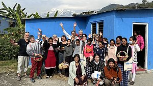Gruppenfoto einer Projektreise in Nepal, Unterstützende und Projektteilnehmende mit einem blauen Gebäude und dem Himalaya im Hintergrund.