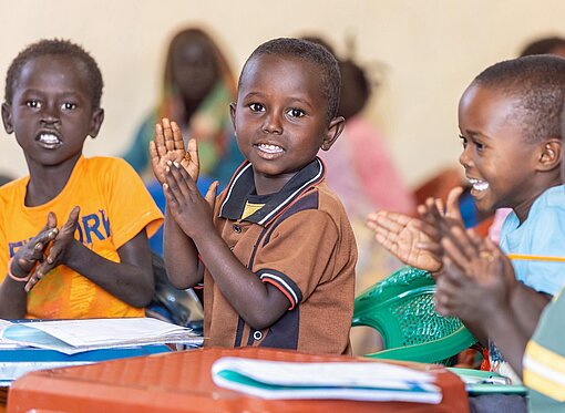 Kinder sitzen in einer Schulbanl mit Schulheften auf dem Schreibtisch