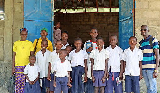 Eine Gruppe Schulkinder und ihre Lehrer stehen vor einem Gebäude mit chrstlichem Kreuz auf der Tür
