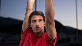 Sportler Riccardo Klotz streckt die Arme in die Höhe und schaut konzentriert nach oben. Er trägt ein rotes Shirt.