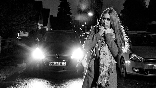 Zekiya stellt dar, wie sie sich nachts allein im Viertel fühlt. Zekiya steht ängstlich im Scheinwerferlicht eines Autos.