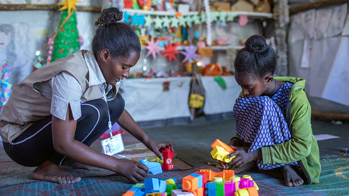 Ein Mädchen und eine Frau sitzen auf dem Boden und spielen mit Bauklötzen.
