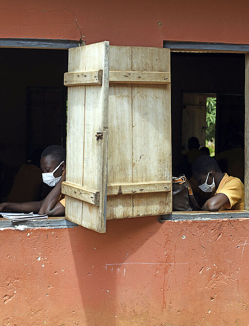 Blick auf zwei offene Fenster eines Klassenzimmers. Darin sitzen Schüler:innen mit Masken und lesen konzentriert.