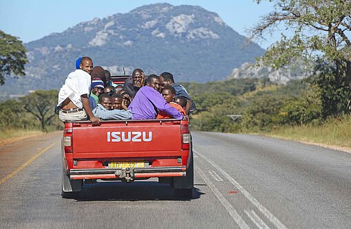 Ein roter Pick-up fährt über eine Straße und transportiert Menschen