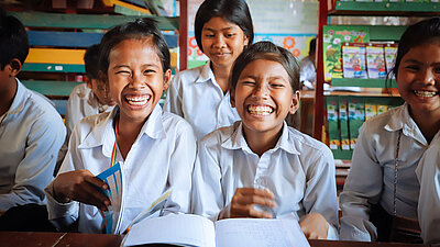 Bild: Zwei Mädchen aus Kambodscha sitzen im Klassenraum und strahlen in die Kamera