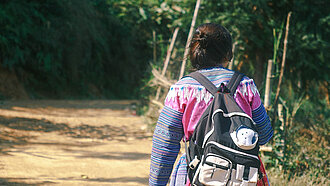 Mädchen mit Rucksack geht einen Weg entlang, Foto von hinten