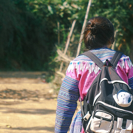 Mädchen mit Rucksack geht einen Weg entlang, Foto von hinten