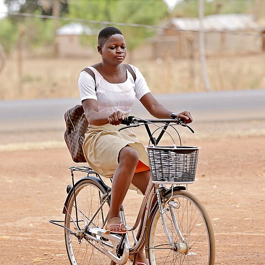 Ein Mädchen in Schuluniform sitzt mit einem Rucksack auf dem Rücken Fahrrad.
