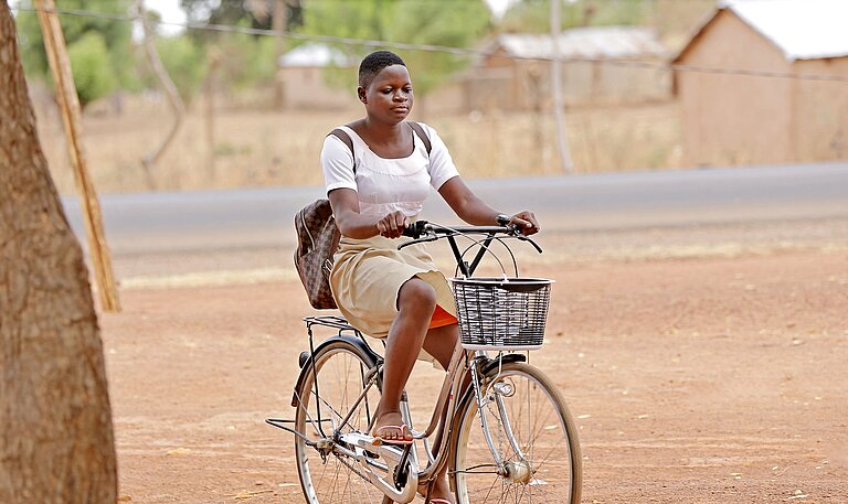 Ein Mädchen in Schuluniform sitzt mit einem Rucksack auf dem Rücken Fahrrad.