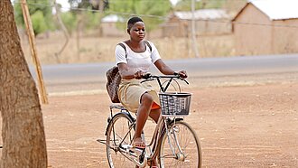 Ein Mädchen in Schuluniform sitzt mit einem Rucksack auf dem Rücken Fahrrad.