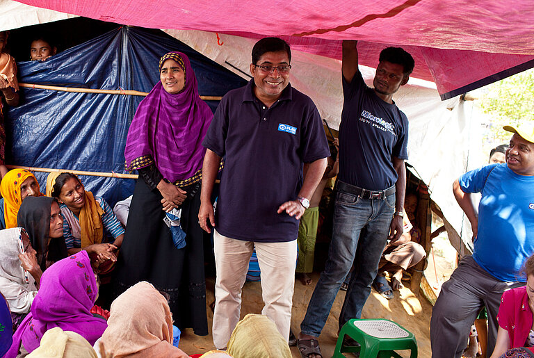 Plan Mitarbeiter steht mit Flüchtlingen in einem Zelt.