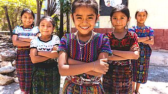 Eine Gruppe von Mädchen aus Guatemala mit bunten Kleidern steht in einem Dreieck. Alle haben ihre Arme vor der Brust verschränkt und lächeln entschlossen.
