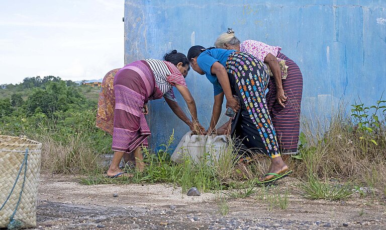 Drei Frauen in bunter Kleidung beugen sich zu einem Brunnen