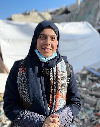 Judie vor einem Trümmerhaufen und einem Zelt in Gaza Judie steht vor einem Trümmerhaufen und einem Zelt im Geflüchtetencamp in Gaza