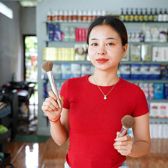 Eine junge Asiatin in rotem T-Shirt steht inmitten eines Friseursalons und schaut in die Kamera