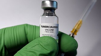 Eine Hand mit Einmalhandschuh hält eine Ampulle mit Impfstoff für Tuberkulose
