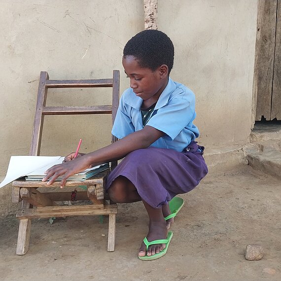 Ein Mädchen macht ihre Schulaufgaben auf einem Stuhl