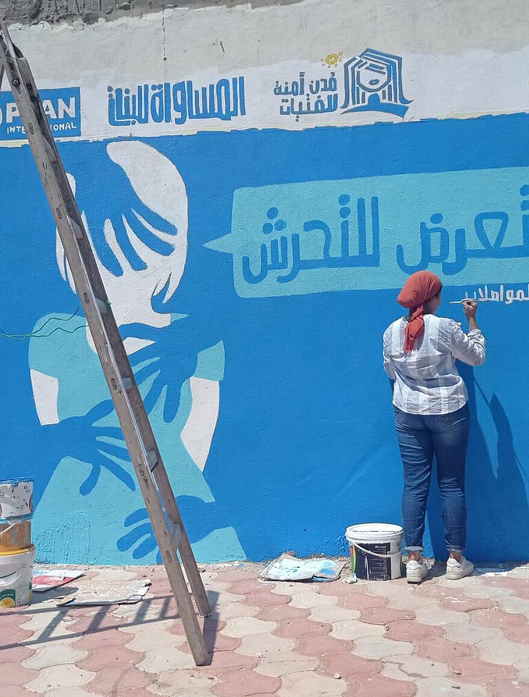 Eine Frau malt ein Wandgemälde mit blauen Farben. 