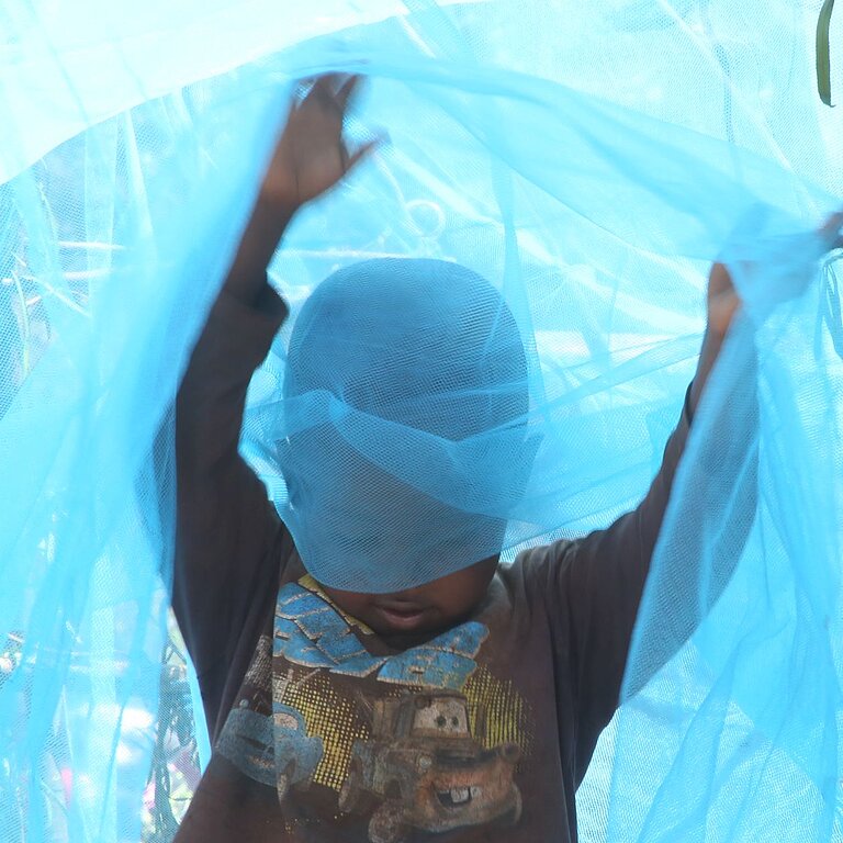 Junge in Ruanda spielt mit Moskitonetz