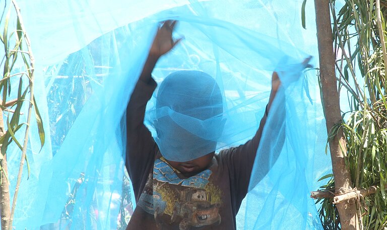 Junge in Ruanda spielt mit Moskitonetz