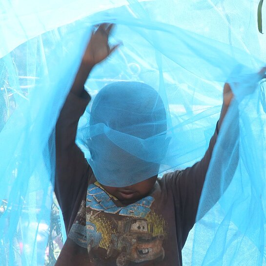 Junge in Ruanda spielt mit Moskitonetz