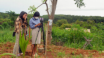 Zwei Mädchen stehen im Freien hinter einem Stativ, auf dem ein Handy befestigt ist.