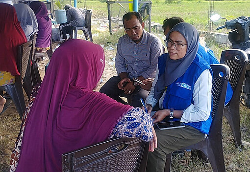 In einem großen Zelt sitzen Menschen auf Plastikstühlen und unterhalten sich