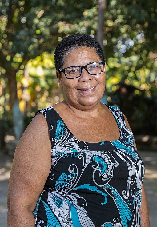 Frau mit kurzen Haaren und Brille vor einer grünen Palmenlandschaft