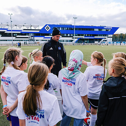 Eine Gruppe Mädchen steht auf einem Trainigsplatz vom HSV und sprechen mit einem Spieler.