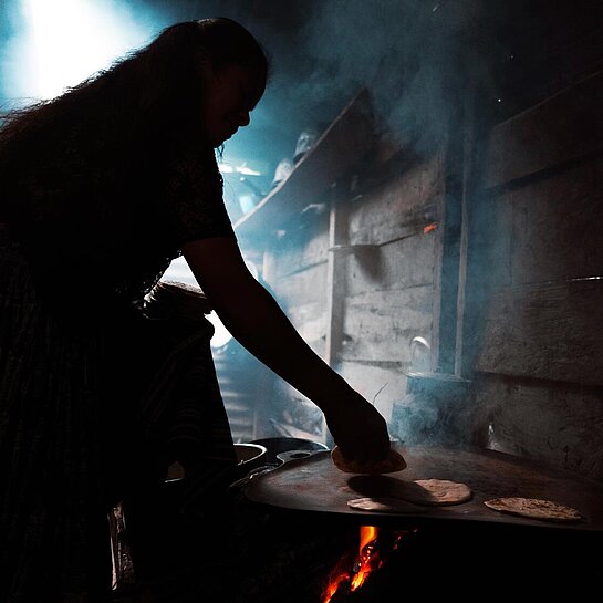 Eine Frau steht am Herd und backt Tortillas.