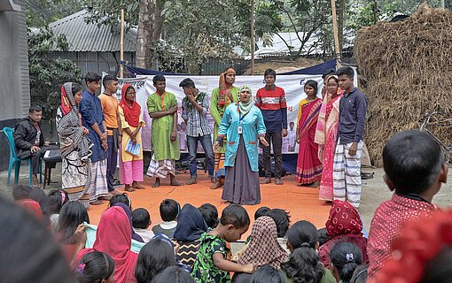Mit Theateraufführungen unterhalten junge Clubmitglieder die Dorfbevölkerung im Norden von Bangladesch und informieren über ihre Sorgen und Nöte Eine Jugendgruppe auf der Bühne vor Publikum