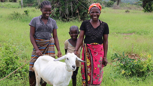 Eine Familie steht mit ihrer Ziege auf einer Wiese.