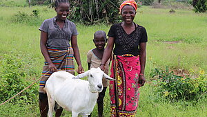 Eine Familie steht mit ihrer Ziege auf einer Wiese.
