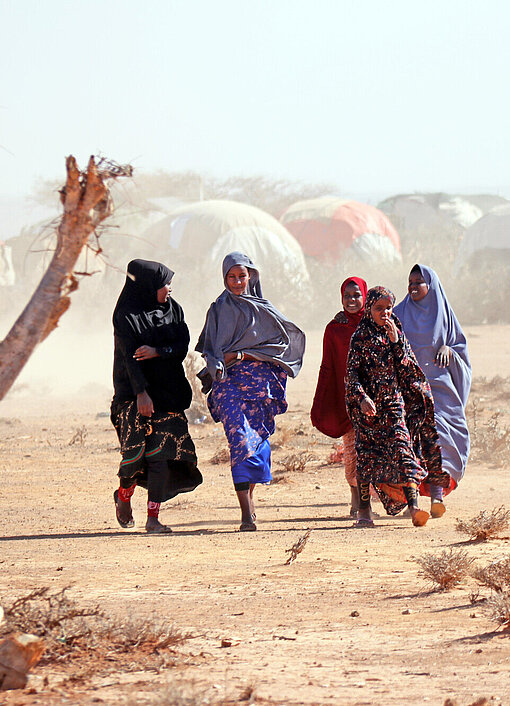 Warum trifft der Hunger Mädchen und Frauen härter als Jungen und Männer? Eine Gruppe heranwachsender Mädchen läuft durch eine trockene Landschaft, im Hintergrund ist ein Camp mit vielen Zelten zu erkennen