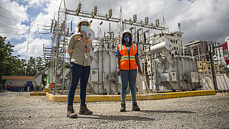 Zwei Frauen in Arbeits-Sicherheitskleidung stehen vor einem Kraftwerk