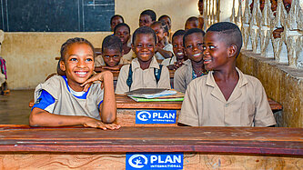 Eine Bankreihe im Klassenzimmer mit Schwarzen Kindern am Schreibtisch