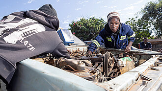 Zwei junge Frauen in Overall beugen sich über den Motorblock eines alten Autos