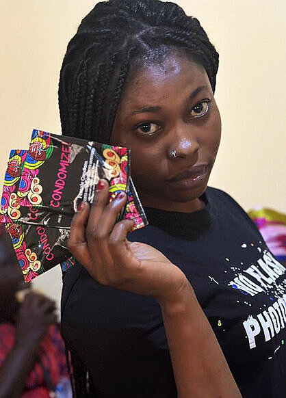 Eine Frau mit drei Frauenkondomen in der Hand blickt selbstbewusst in die Kamera