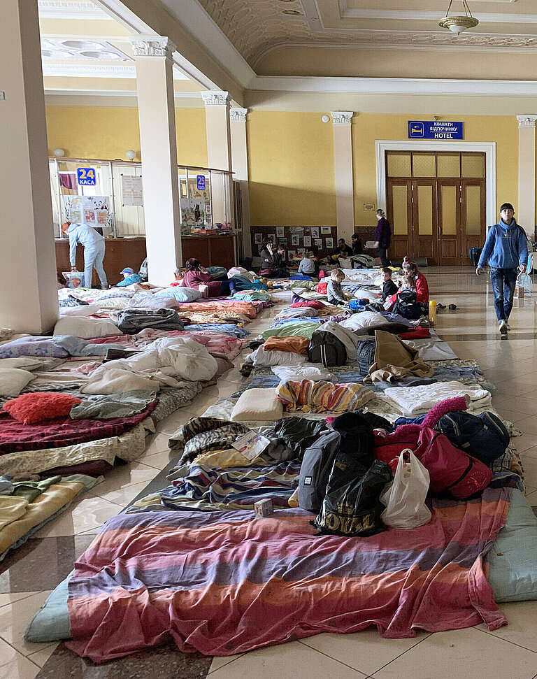 Mehrere Matratzen und Decken liegen nebeneinander auf dem Fußboden in einer Bahnhofshalle
