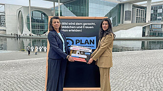 Zwei Frauen stehen mit einem Banner mit dem Logo von Plan-International in Berlin-Mitte vor dem Bundestag