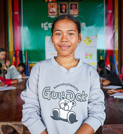 Eine Teenagerin mit Zöpfen sitzt in einem Klassenzimmer zwischen anderen Teenagern