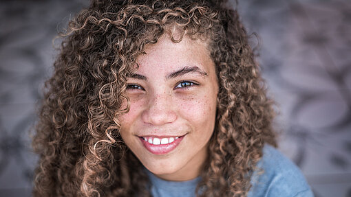 Portrait von der lächelnden Julia mit braunen lockigen Haaren.