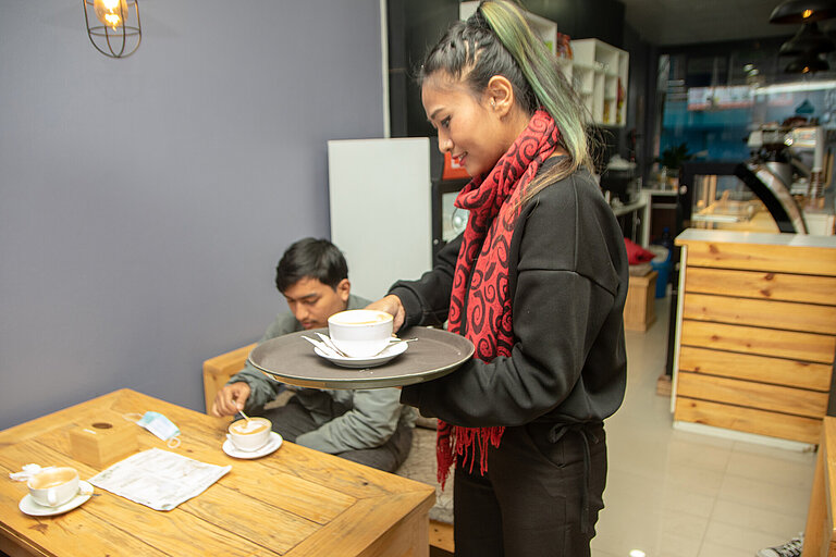 Urmila serviert einem Kunden Kaffee