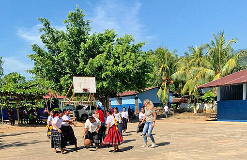 Schülerinnen spielen mit ihrem weitgereisten Gast Basketball Auf einem sandigen Platz zwischen Palmen spielen mehrere Personen Basketball