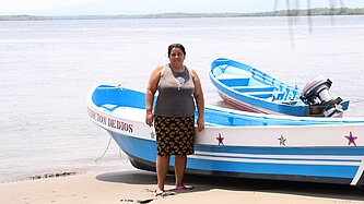 Eine Frau steht am Strand, im Hintergrund ist ein Fischerboot am Ufer zu sehen.